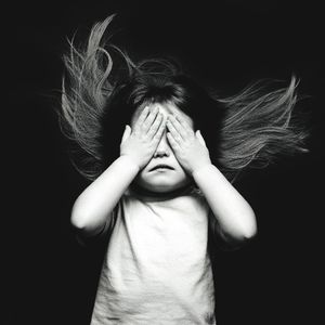Portrait of a girl covering face against black background