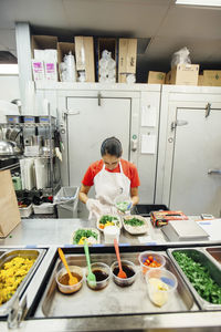 High angle view of female chef serving food in plates on kitchen counter