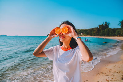 Close-up of smiling woman holding orange fruits at beach