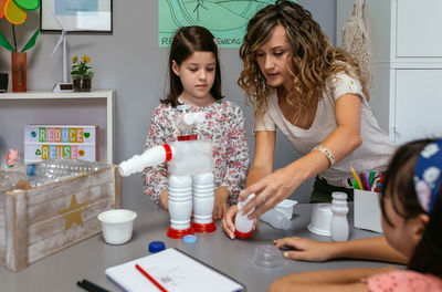 Teacher explaining to children how make recycled toy robot with plastic packages