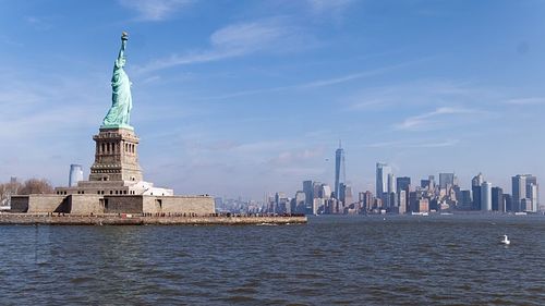 Statue of liberty by river against blue sky