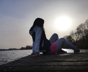 Side view of woman sitting on wood against sky during sunset