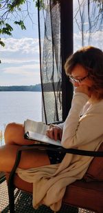 Side view of woman reading while sitting on chair