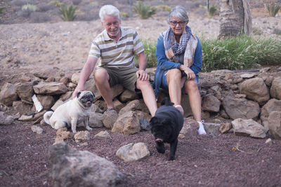 Senior couple sitting on rocks with dogs on ground