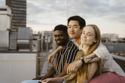 Portrait of smiling man with arms around male and female friends on terrace