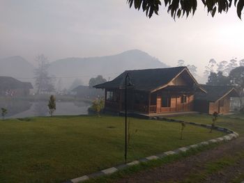 Scenic view of field by houses against sky