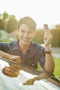 Portrait of happy young man showing key while leaning on car