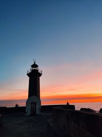 Lighthouse by sea against sky during sunset