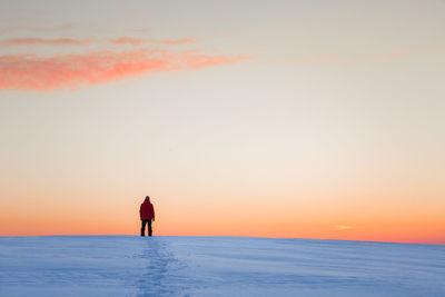 Mid adult man standing on snow covered field against sky during sunset