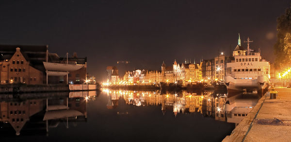 Illuminated buildings by river against sky at night