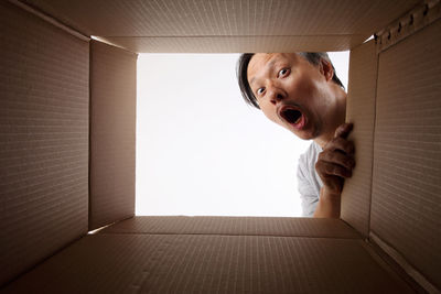 Portrait of shocked man peeking in cardboard box