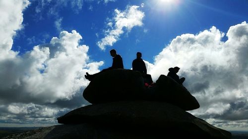 Low angle view of people standing on rocks against cloudy sky