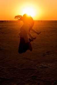 Woman jumping at beach against sky during sunset