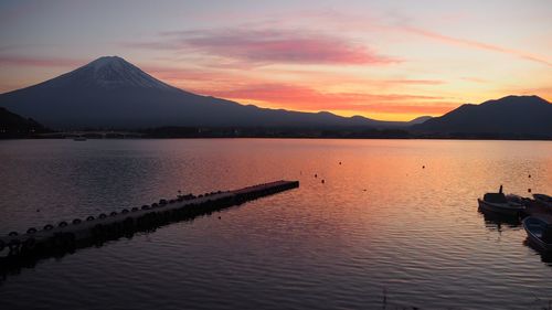 View of a pier amidst lake with mountains in background at dusk