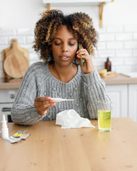 Portrait of smiling young woman using mobile phone while sitting on table