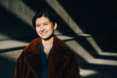 Portrait of smiling young woman standing against wall