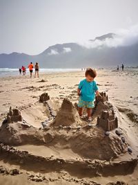 Boy playing with sand castle at beach against sky
