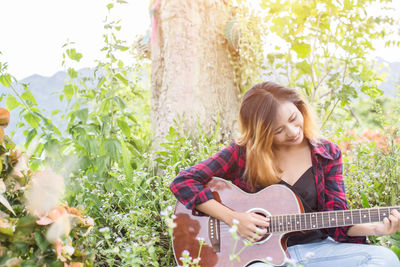 Young woman playing guitar against plants