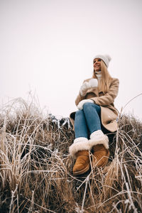 Young woman sitting on hay against clear sky