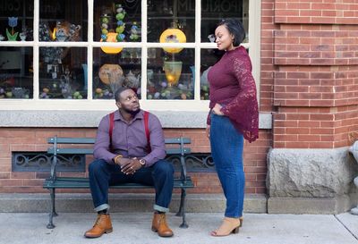 Full length of woman standing by man sitting on bench