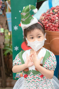 Positive thai asian girl little preschooler child in green christmas tree hat wearing 3d face mask.