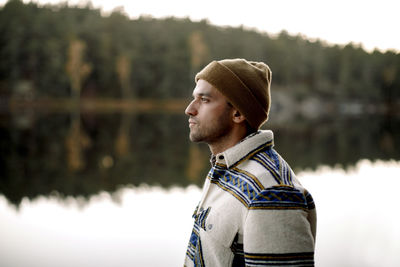 Thoughtful man in knit hat standing by lake