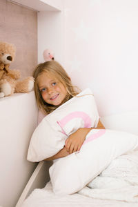 Beautiful girl hugs a pillow on the bed in the nursery