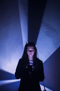 Portrait of young woman using phone against blue sky