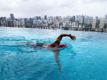 Man swimming in infinity pool against cityscape