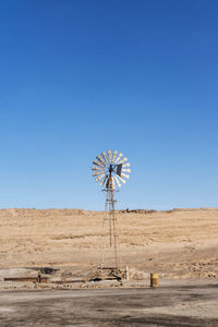 Windmill on desert against clear blue sky