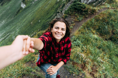 A young smiling woman holds her partner's hand while climbing to the top of the mountain.