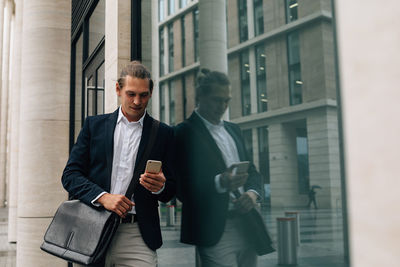 Smiling businessman using smart phone while standing by building