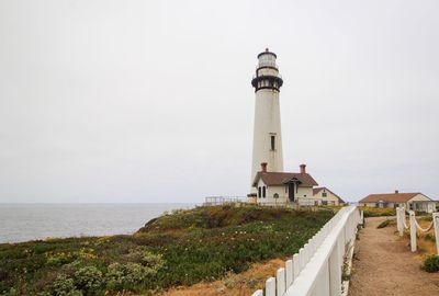 Lighthouse by sea against clear sky