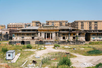 Field by old buildings in circus maximus against clear sky