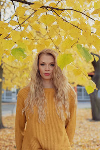 Portrait of young woman standing against autumn tree