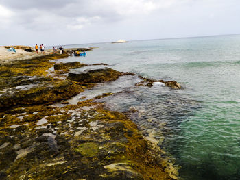 People standing on rock by sea against sky