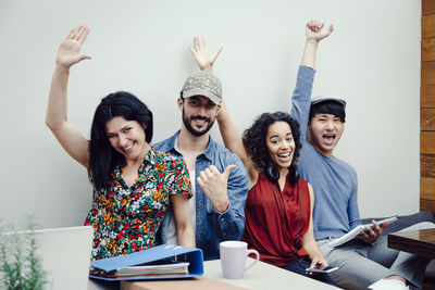 Portrait of cheerful creative business people with hands raised sitting against white wall