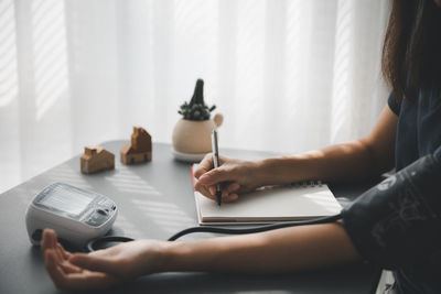 Midsection of woman using smart phone while sitting on table