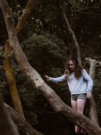 Woman standing on tree trunk in forest