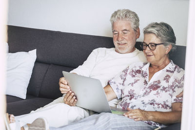 Senior couple looking at laptop while sitting on sofa in living room
