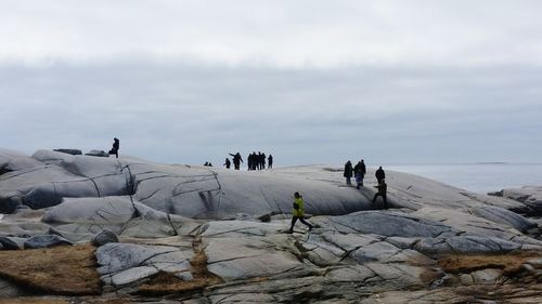 People on rock formation by sea against sky at peggys cove