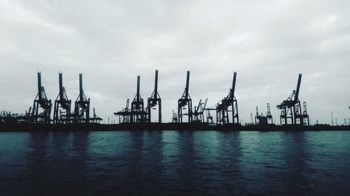 Cranes at commercial dock against sky