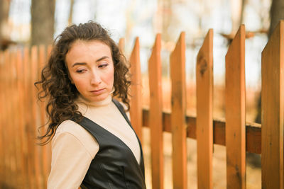 Portrait of young woman standing against fence