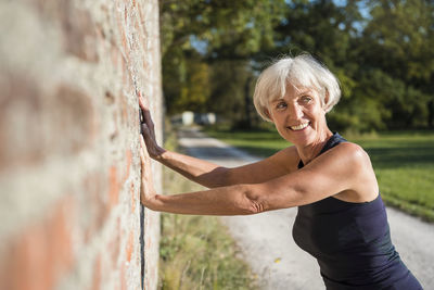 Smiling sportive senior woman leaning against a brick wall
