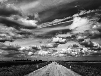 Road by agricultural field against storm clouds