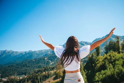 Rear view of woman standing on mountain against clear blue sky