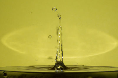 Close-up of drop falling in water against yellow background