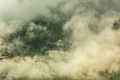 Low angle view of house between clouds against mountain