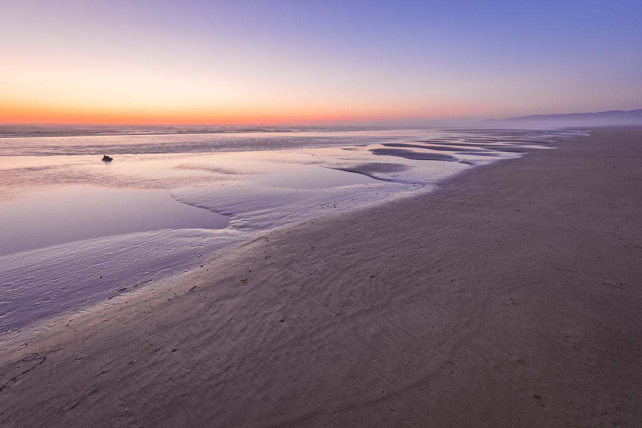 sunset, scenics, tranquil scene, tranquility, beauty in nature, sea, idyllic, clear sky, nature, water, majestic, travel destinations, remote, non-urban scene, orange color, dramatic sky, mountain, calm, blue, tourism, seascape, outdoors, sky, moody sky, vacations, wave pattern, no people