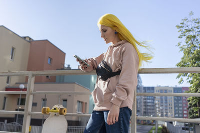 Young woman using smart phone against sky